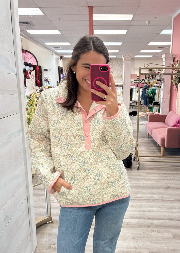 Woman taking a mirror selfie in a store wearing a floral top and jeans.