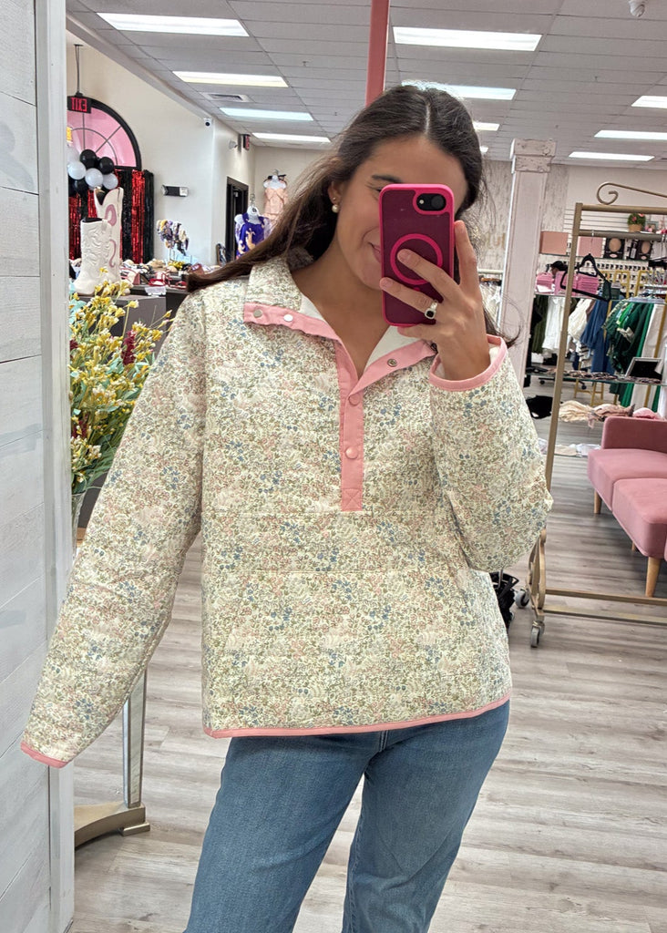 Woman taking a mirror selfie wearing a floral top and jeans in a store.