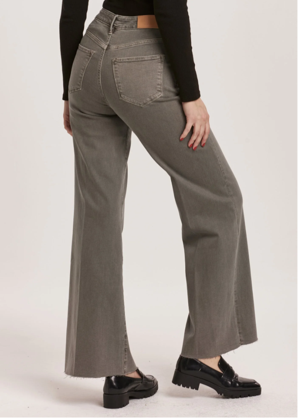 Person wearing gray flared jeans and black shoes on a white background