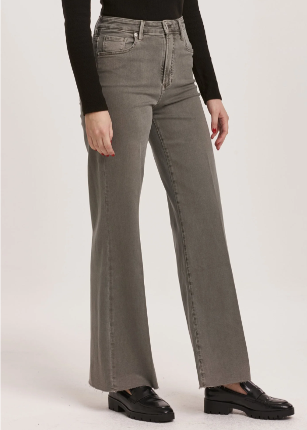 Person wearing gray flared jeans and black top on a white background