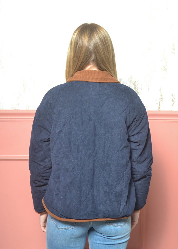 Person wearing a blue quilted jacket with brown trim against a pink wall.