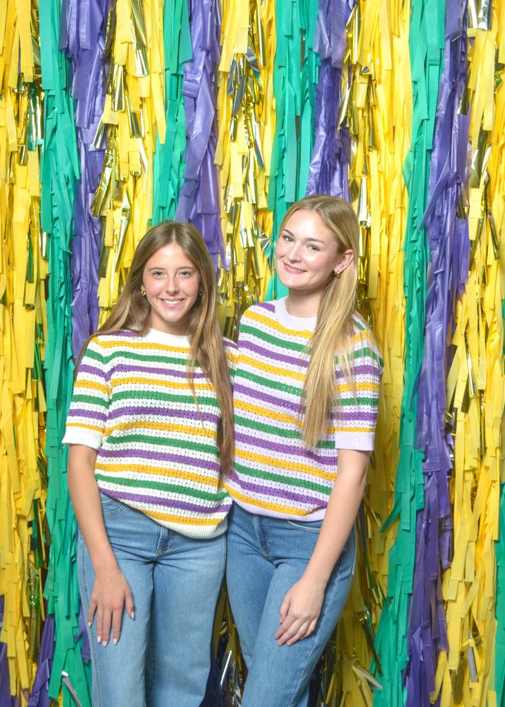 Two people wearing striped shirts standing in front of a colorful paper streamer backdrop.