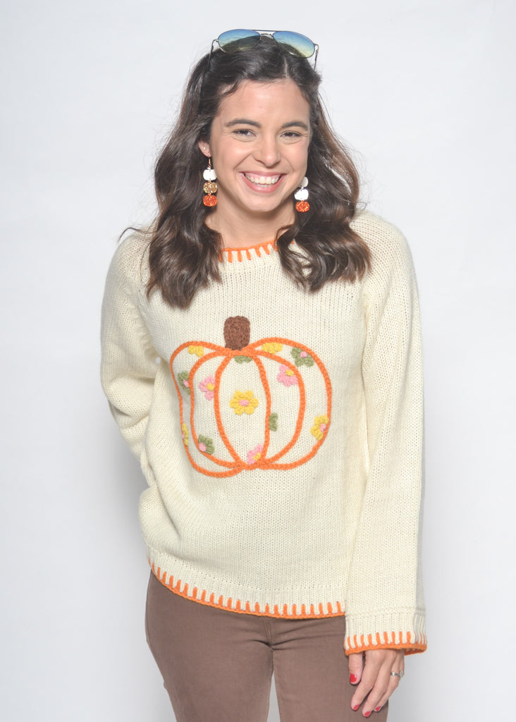 Woman wearing a cream sweater with a pumpkin design on a white background