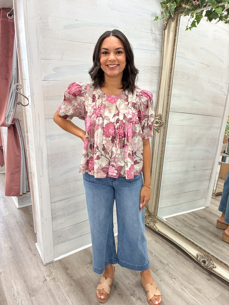 Woman wearing a floral blouse and jeans standing in a clothing store.