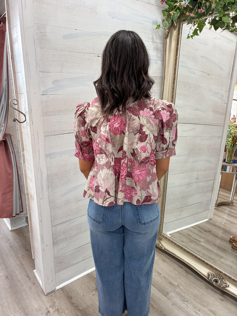 Person wearing a floral blouse and blue jeans standing in front of a mirror.