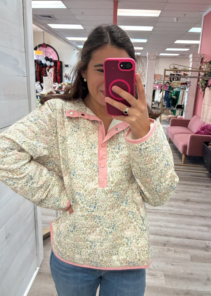 Woman taking a mirror selfie wearing a floral blouse with pink trim in a store.